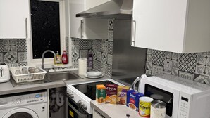 Une cuisine moderne avec des meubles blancs, une hotte en acier inoxydable, un lave-vaisselle, une machine à laver et un four à micro-ondes.