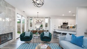 Ein modernes Wohnzimmer mit Kamin, zwei grüne Sessel, einem blau-weißen karierten Teppich und einem hellblauen Sofa.