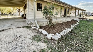 Una casa de un piso con porche cubierto, un pequeño jardín con un árbol joven y un camino de entrada de grava.