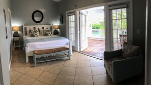 A bedroom with a bed, bedside tables, a bench, a chair, and a view of the outdoors through a sliding glass door. - Gorgeous Coral Lagoon Villa - Top Rated Resort in Marathon w/ Boat Slip -Amazing (Marathon)