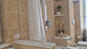 Ein modernes Badezimmer mit einer Badewanne, einer Dusche und einem Waschbecken. Die Wände sind mit dekorativen Fliesen versehen und über dem Waschbecken hängt ein Spiegel.