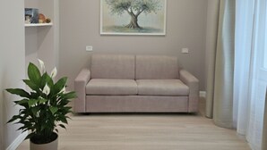 Ein Wohnzimmer mit einem beigefarbenen Sofa, einem Topf mit Pflanze, einem Baumgemälde und einer Klimaanlage an der Wand.