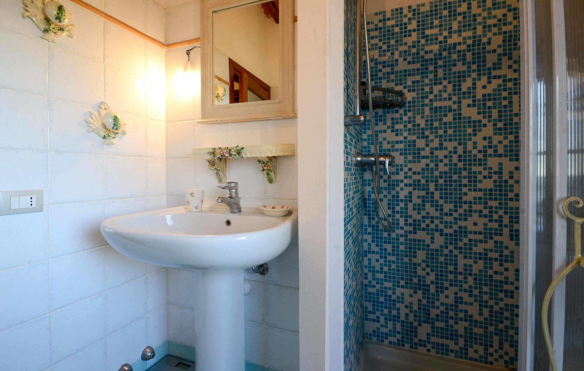 A bathroom with a white sink, a mirror, and a shower with blue mosaic tiles.