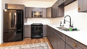 Una cocina moderna con armarios oscuros, un refrigerador de acero inoxidable, un horno empotrado y un lavamanos con grifo.