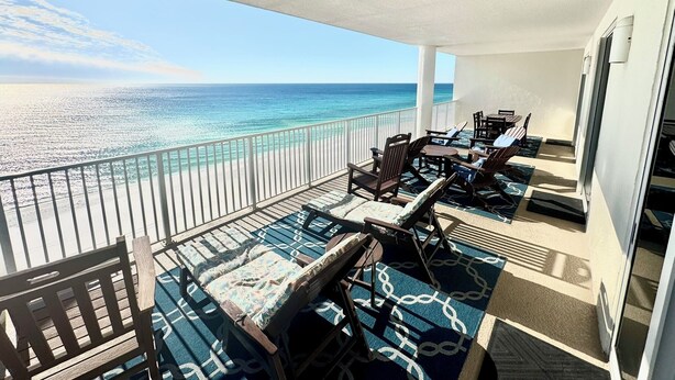 A balcony with a view of the ocean, furnished with wooden chairs and tables, and a patterned rug. - Direct Beachfront, Largest Balcony,4BR-4Ba, Bunks, 2 Master Beds, Full Remodel (Panama City Beach)