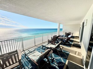 En balkon med udsigt over havet, møbleret med træstole og borde samt et tæppe med et mønster.