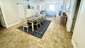 A dining area with a table and chairs, a chandelier, and a patterned rug. - Direct Beachfront, Largest Balcony,4BR-4Ba, Bunks, 2 Master Beds, Full Remodel (Panama City Beach)