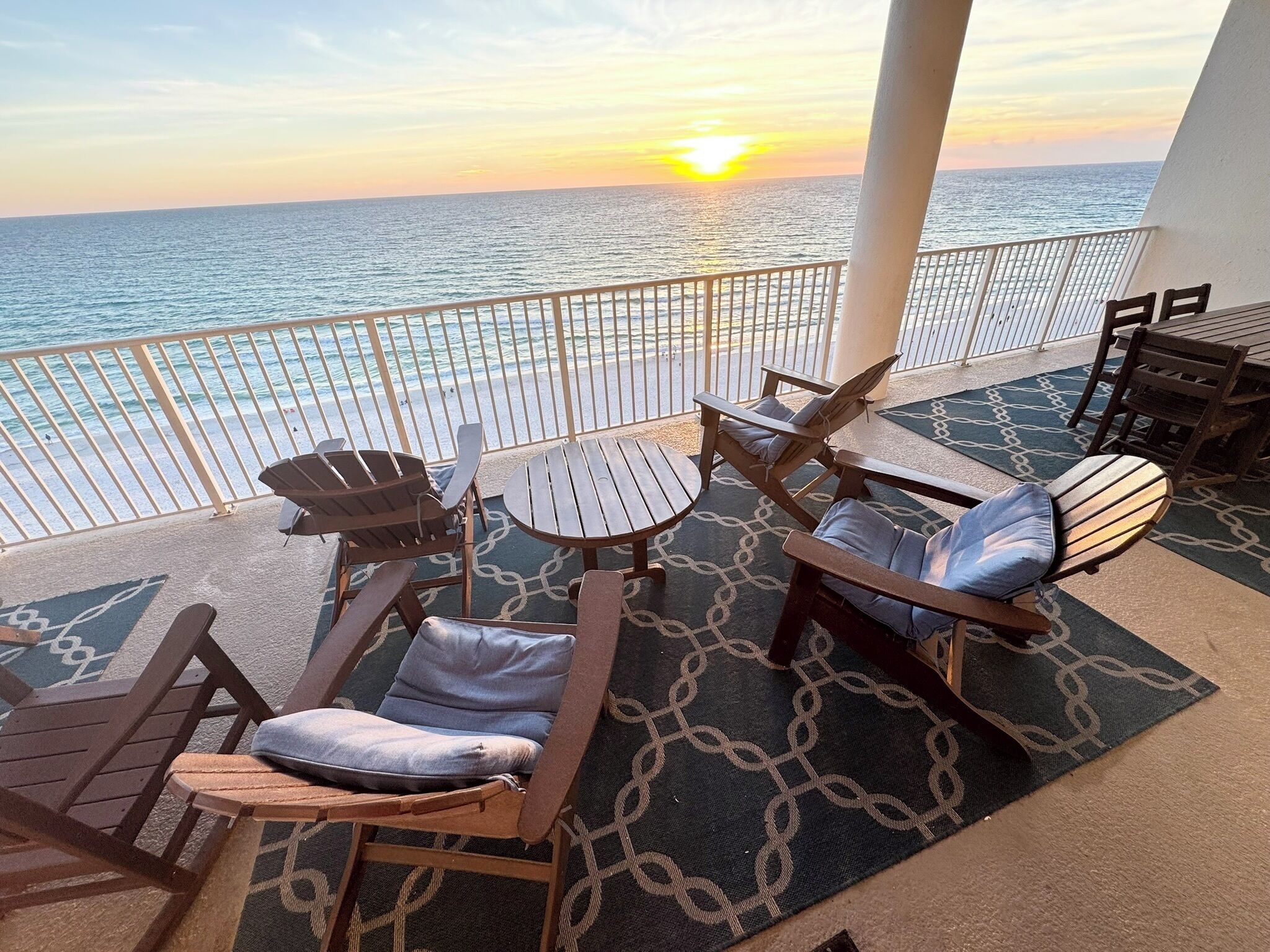 Eine Terrasse mit Sitzgelegenheiten, Blick auf das Meer und ein Sonnenuntergang.