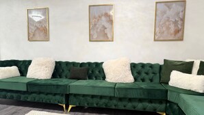 Ein grünes Modulsofa mit Karopracht, weiße und dunkelgrüne Zierkissen sowie goldfarbene Füße. Darüber an der Wand hängen drei abstrakte Gemälde.