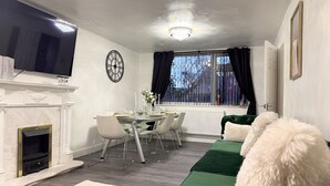 Ein modernes Wohnzimmer mit Kamin, Esstisch und grünem Sofa.