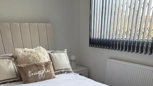 Ein Schlafzimmer mit einem großen Bett, einem Kopfteil, einem Nachttisch, einem Fenster mit Jalousien und einer Heizung.