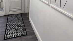Ein Flur mit einer weißen Tür, einem gemusterten Teppich und drei gerahmten abstrakten Kunstwerken an der Wand.
