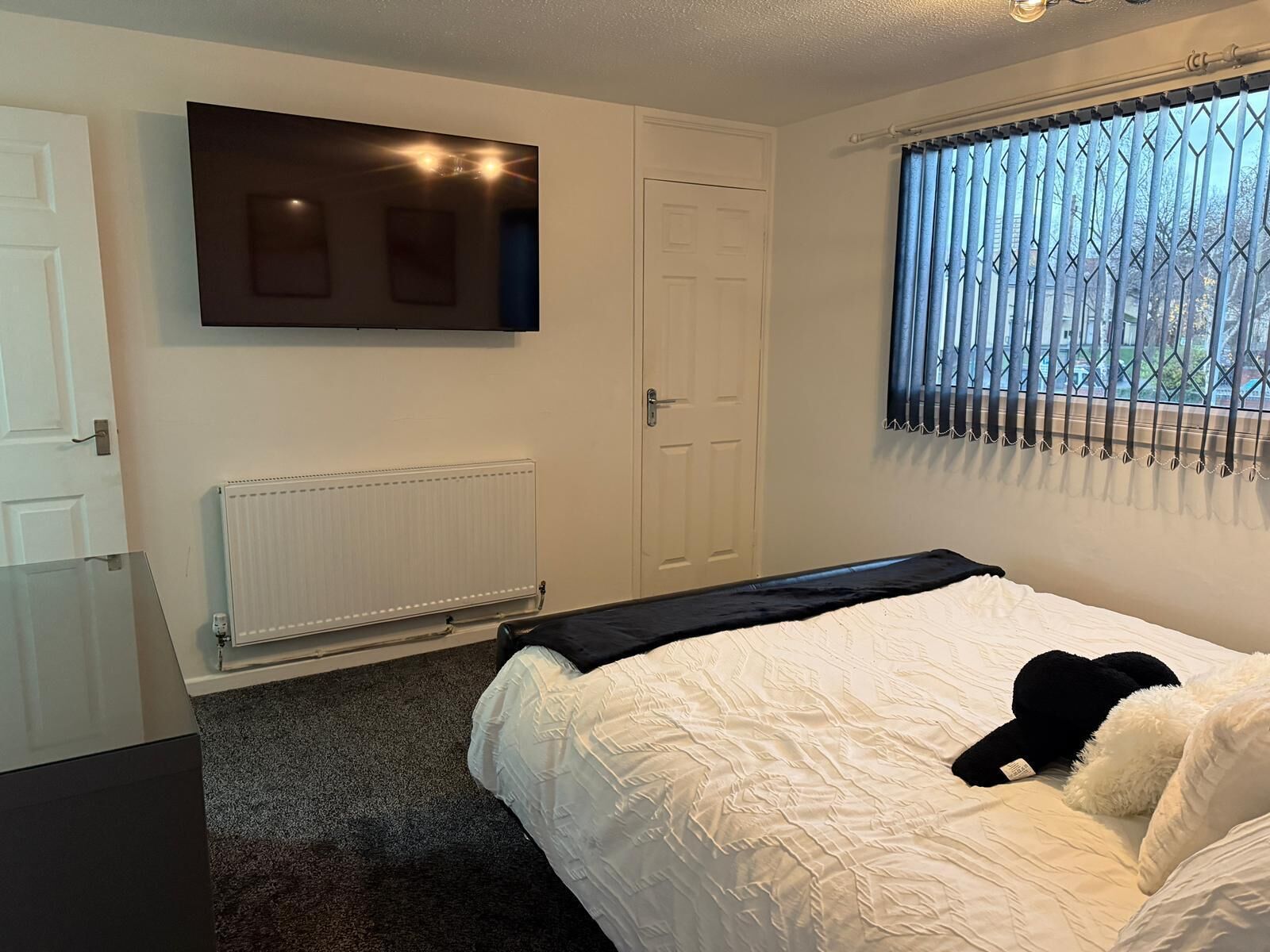 Ein Schlafzimmer mit Bett, Heizkörper, Tür und Fenster mit Jalousien.