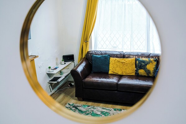 A room with a brown leather sofa, a small desk, and a window with yellow curtains. - Large Modern 5-Bed House (Westhoughton)
