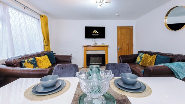 Una sala de estar moderna con chimenea, sofás de cuero, una mesa de comedor con vajilla azul y blanca, y un televisor montado.