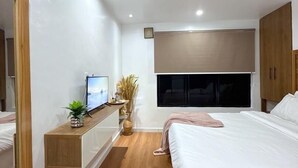 Een moderne slaapkamer met een bed, nachtkastje, televisie en een groot raam.