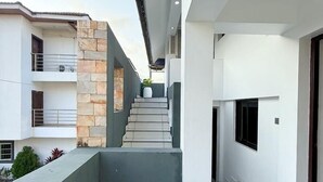 Een modern woongebouw met een centrale trap die leidt naar een balkon, omringd door witte muren en stenen accenten.