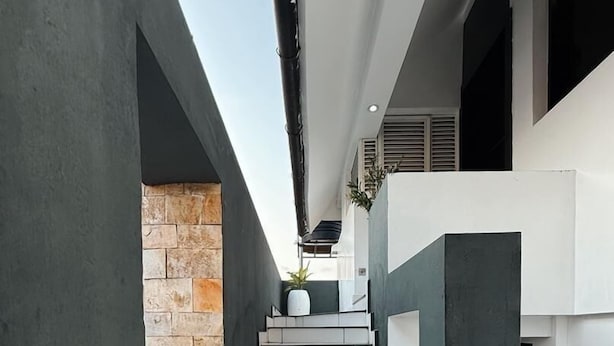 Een moderne trap met witte tegels en een metalen leuning, leidend naar een balkon met een stenen muur en een plant in een pot.