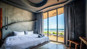 A modern bedroom with a large bed, a wooden bench, and a view of the ocean. - BT Homes - Tankah Luxe (Tulum)