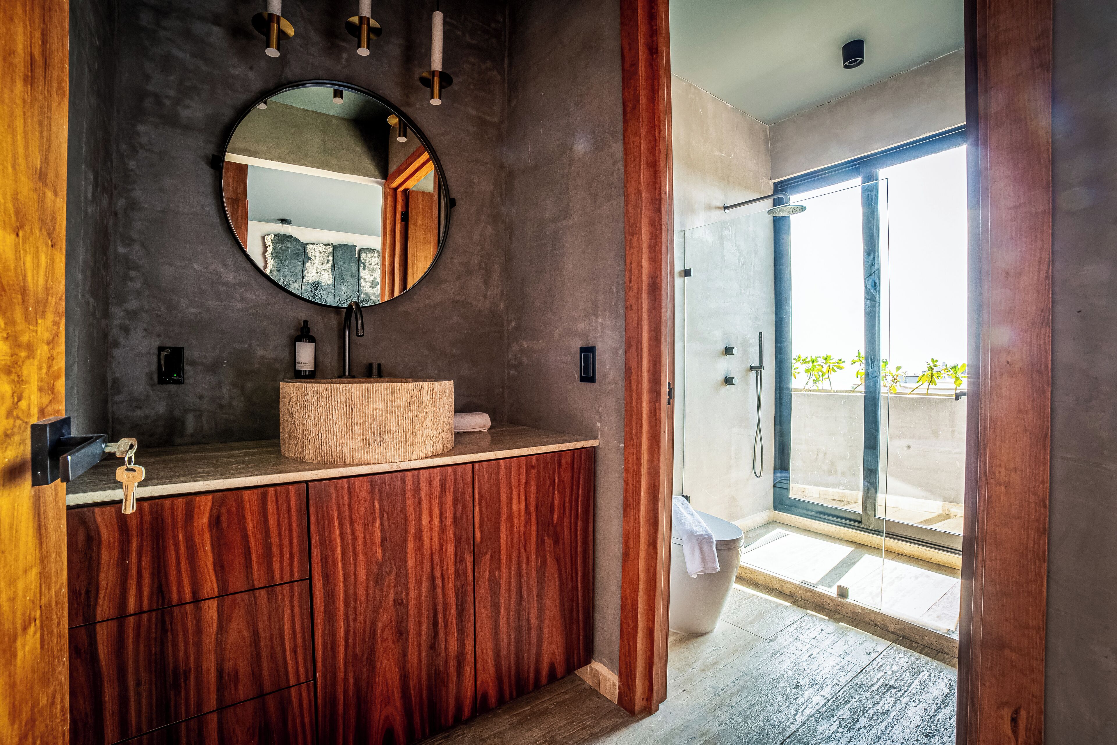 Un baño moderno con tocador de madera, un espejo redondo y mampara de ducha de vidrio.