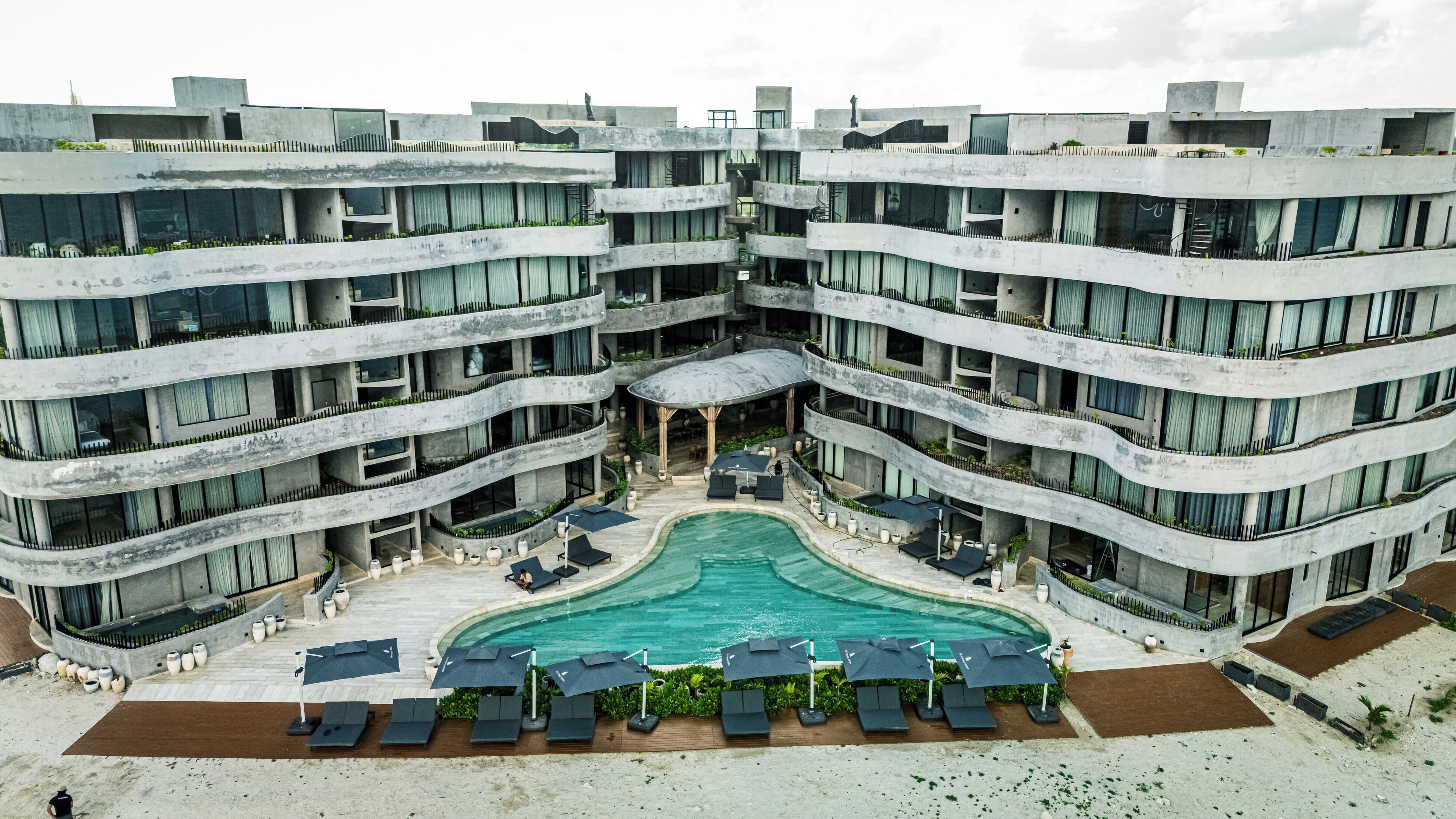 Un hotel de varios pisos con piscina central, mobiliario exterior y balcones.