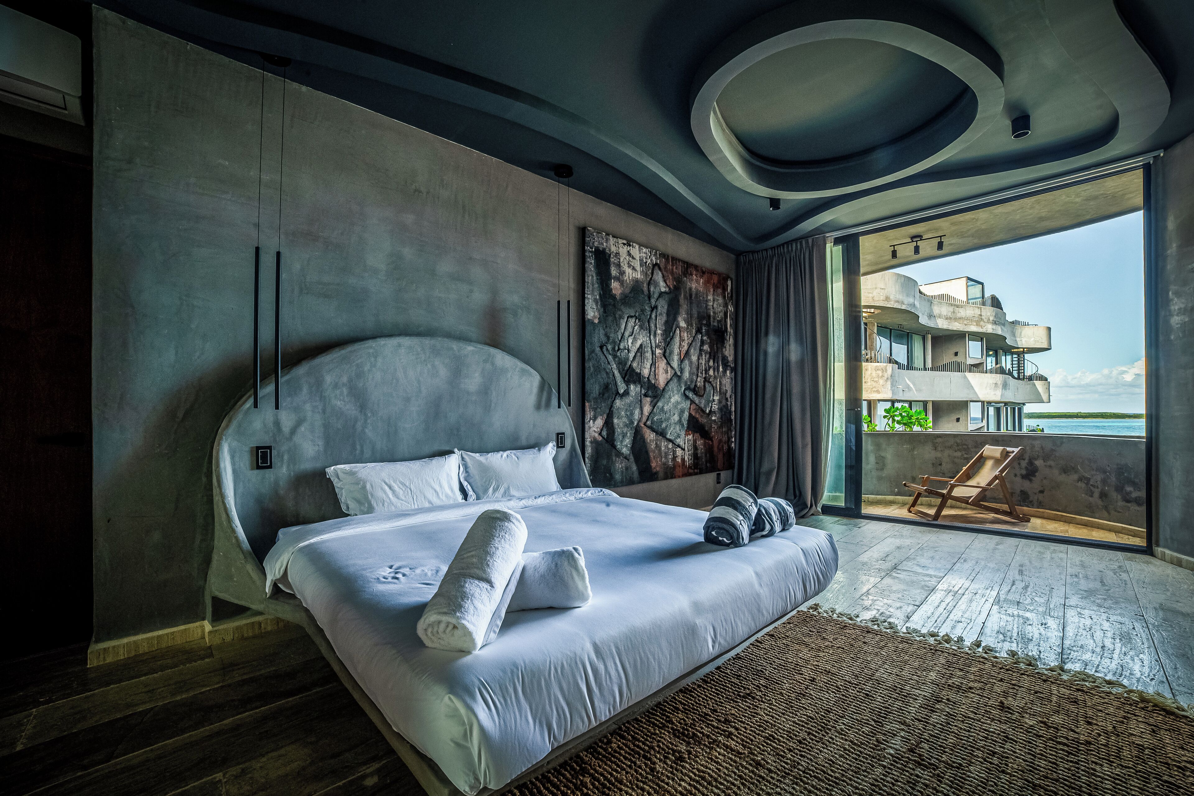 Ein modernes Schlafzimmer mit einem großen Bett, Blick auf ein Gebäude durch eine Glastür und Holzboden.
