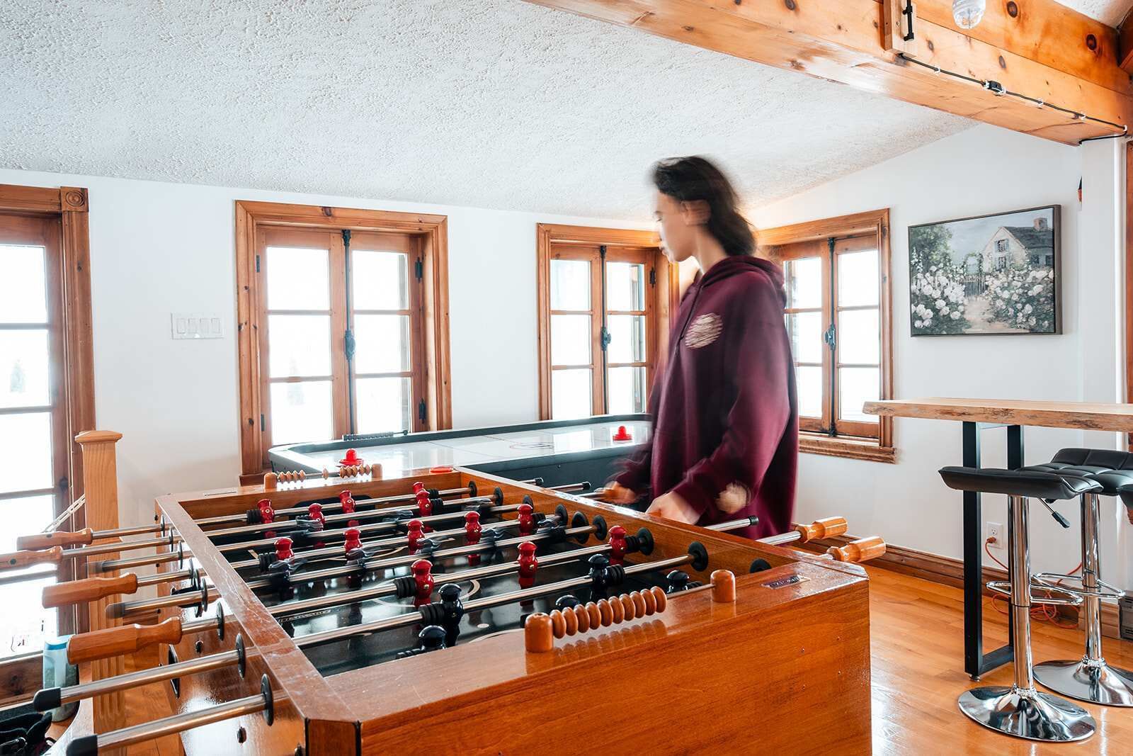 A room with a foosball table, wooden windows, and a painting on the wall.