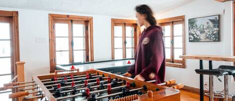 A room with a foosball table, wooden windows, and a painting on the wall.
