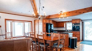 A spacious kitchen with wooden cabinets, a large island, and a dining area with a wooden table and chairs. - Le Repere du Lac - Lake View, Access, beach & Spa (Venise-en-Québec)