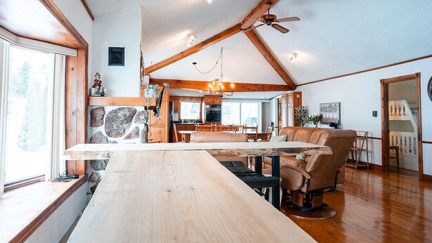 A spacious living area with a wooden dining table, a sofa, and a ceiling fan. - Le Repere du Lac - Lake View, Access, beach & Spa (Venise-en-Québec)