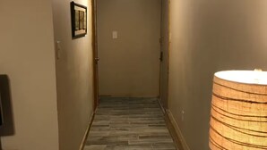 Un couloir avec un plancher en bois, une lampe et une poubelle.