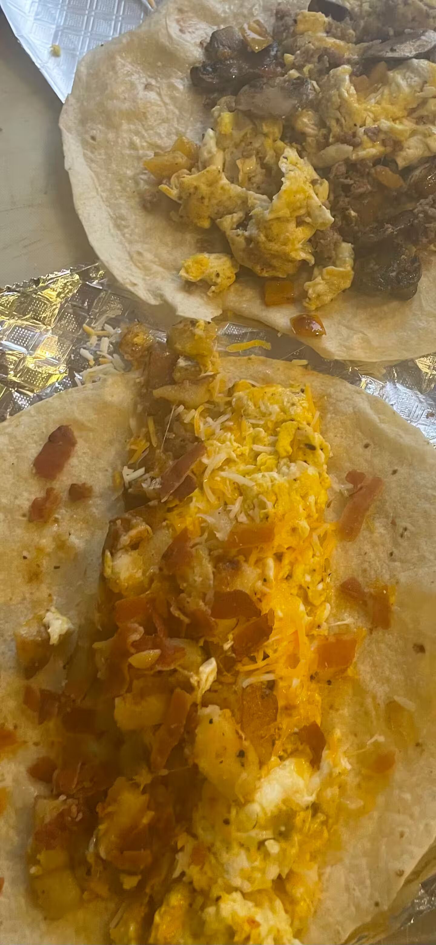 A meal consisting of two tacos with scrambled eggs and bacon, served on a foil-lined tray.