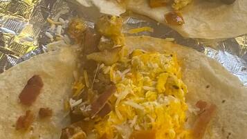 A meal consisting of two tacos with scrambled eggs and bacon, served on a foil-lined tray.