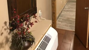 Un couloir avec une porte en bois, un climatiseur blanc et une plante en pot ornée de fleurs rouges.