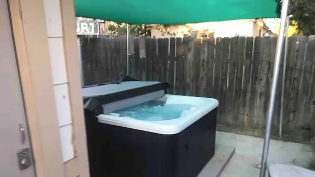 Un bain à remous dans un jardin, avec une clôture en bois et une tonnelle verdoyante.