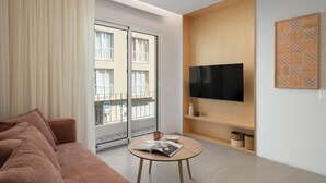 A modern living room with a sofa, a coffee table with a magazine, a TV on a wooden wall, and a balcony with a view of buildings. - With patio, in Funchal city centre - AL'gria I (Funchal)