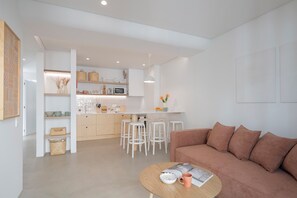 Ein modernes Wohnzimmer mit einem braunen Sofa, einem runden Couchtisch mit einer Zeitschrift und einer Küchenzeile mit weißen Barhocker und einer weißen Arbeitsplatte.