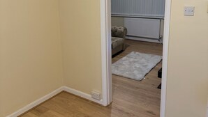 A room with wooden flooring, a radiator, a grey rug, and a beige sofa. - 3-Bed Home, Free Parking, Smart TV,Family & Business Ready (Slough)