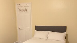 A single bed with a dark headboard and white bedding in a room with beige walls and a carpeted floor. - 3-Bed Home, Free Parking, Smart TV,Family & Business Ready (Slough)