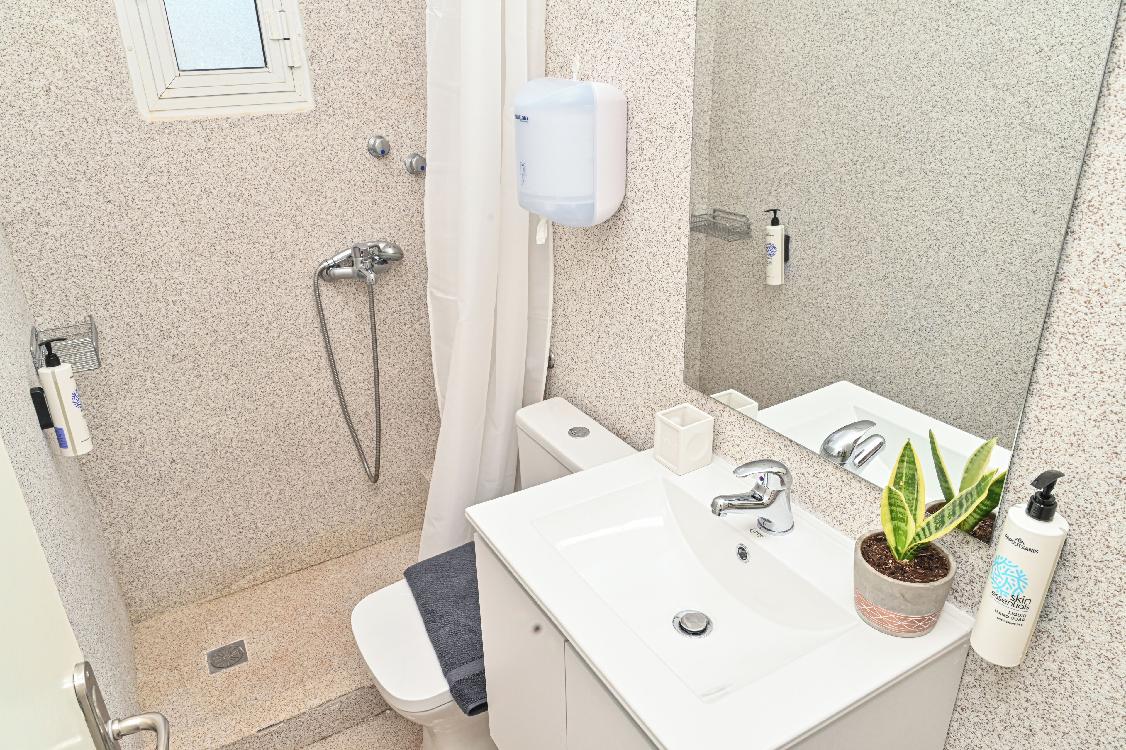 A bathroom with a shower, toilet, sink, and a potted plant.