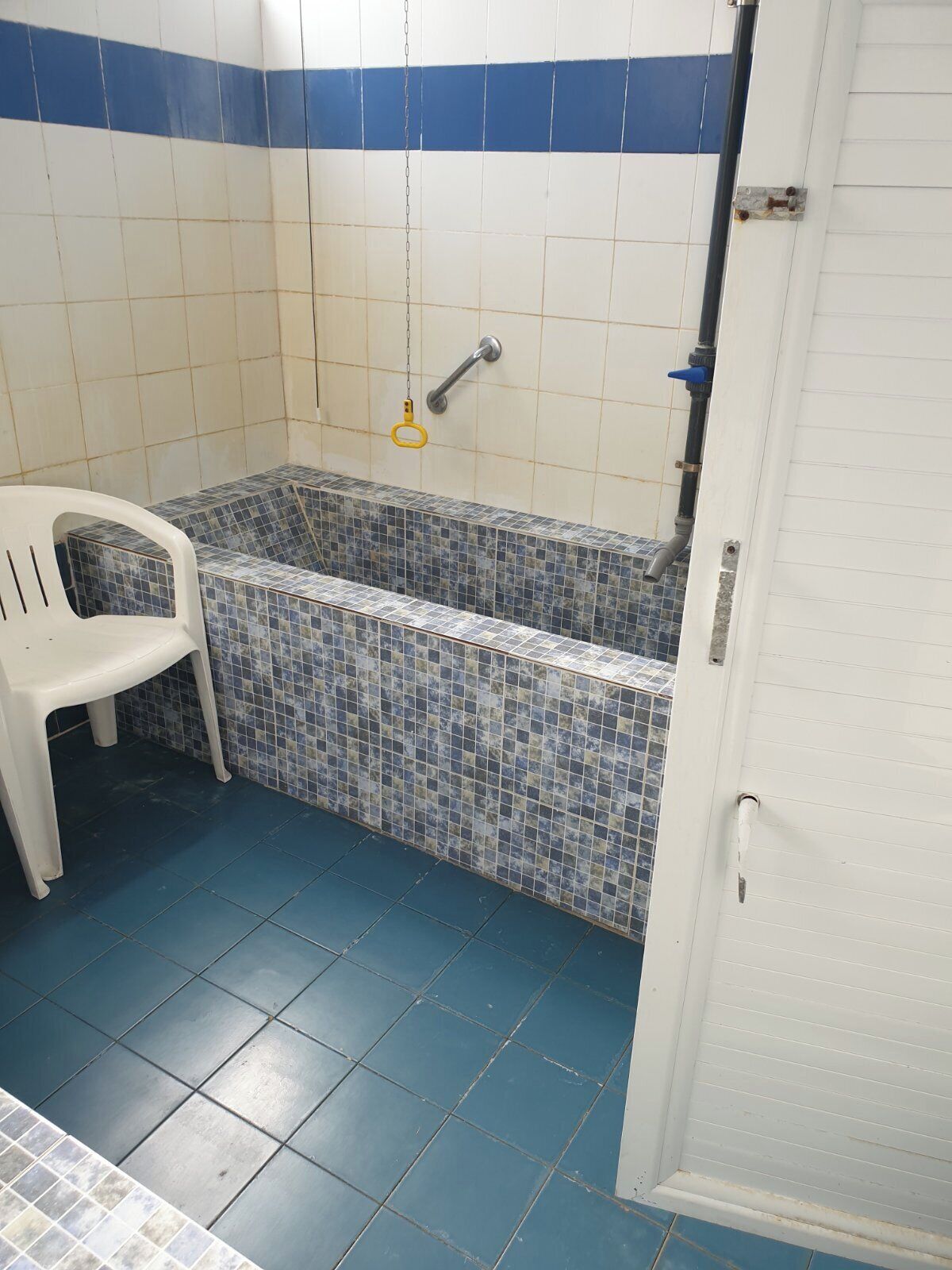 Un baño con una bañera, una silla de plástico blanca y una puerta.