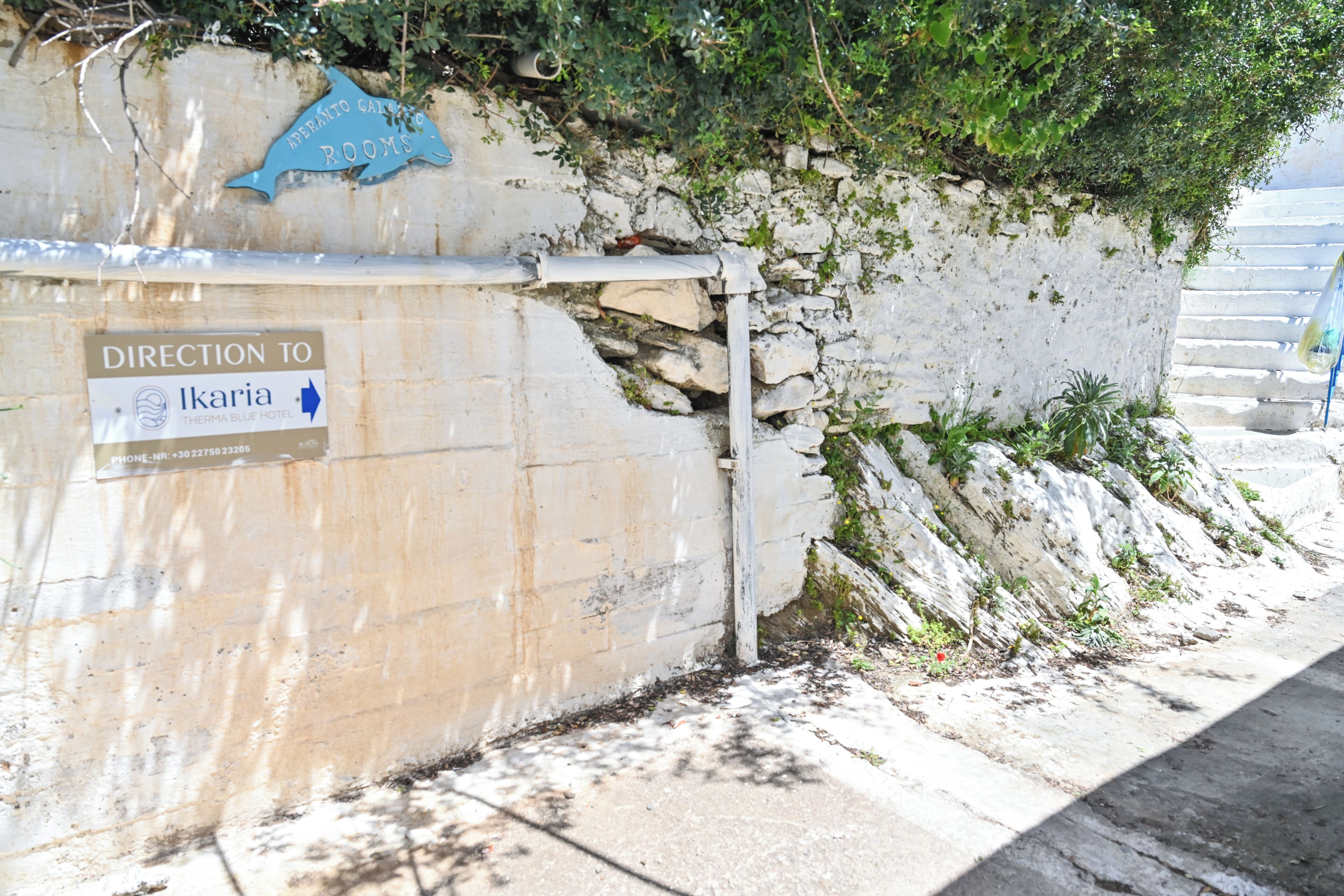 Un mur sur lequel est affiché un panneau indiquant la direction à suivre pour se rendre à Ikaria et à l’hôtel Therma Blue.