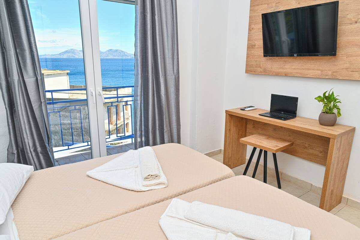 Ein Hotelzimmer mit einem Bett, einem Schreibtisch mit Laptop, einer Pflanze und einem Fernseher.