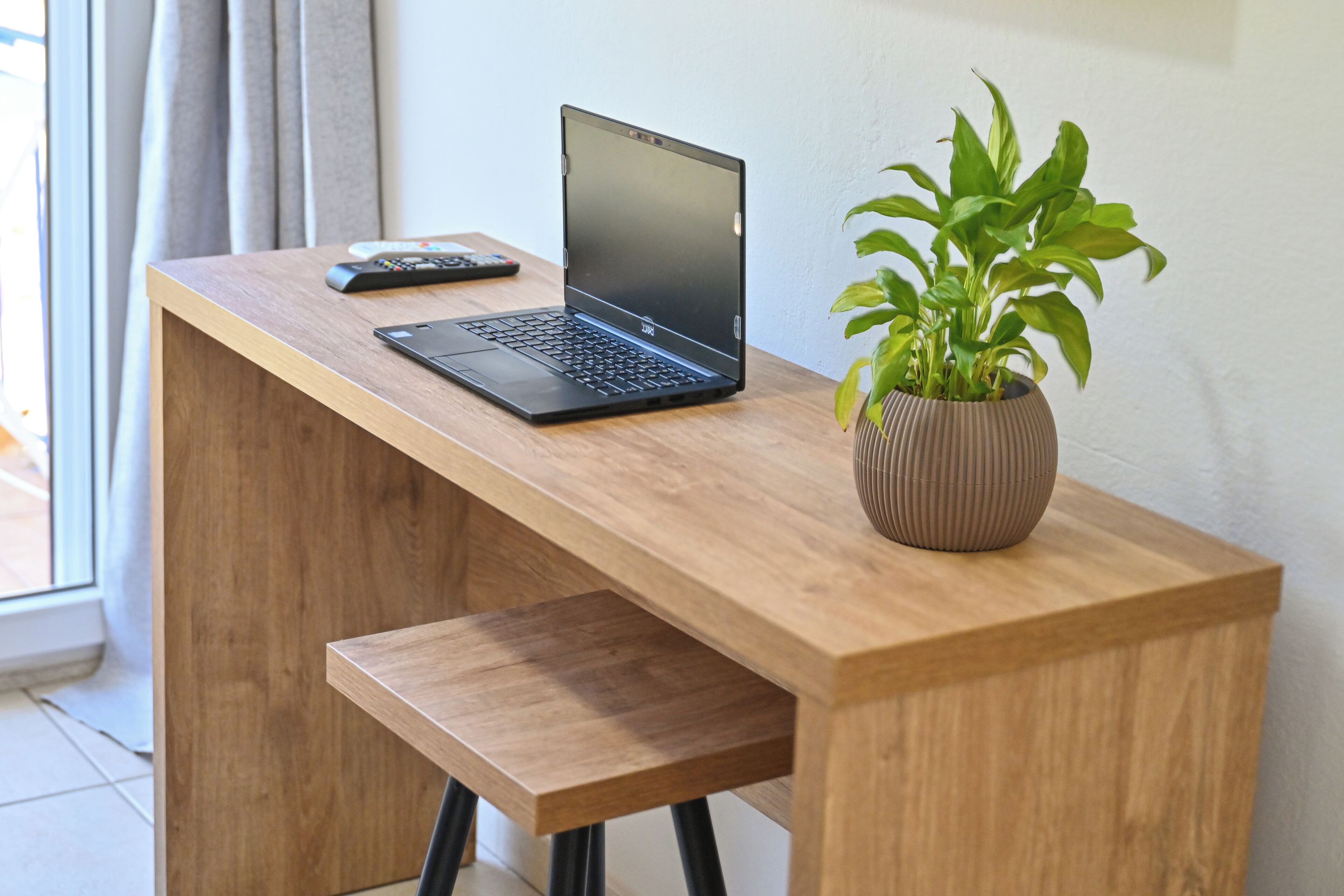 Escritorio de madera con una computadora portátil, un control remoto y una planta en maceta.