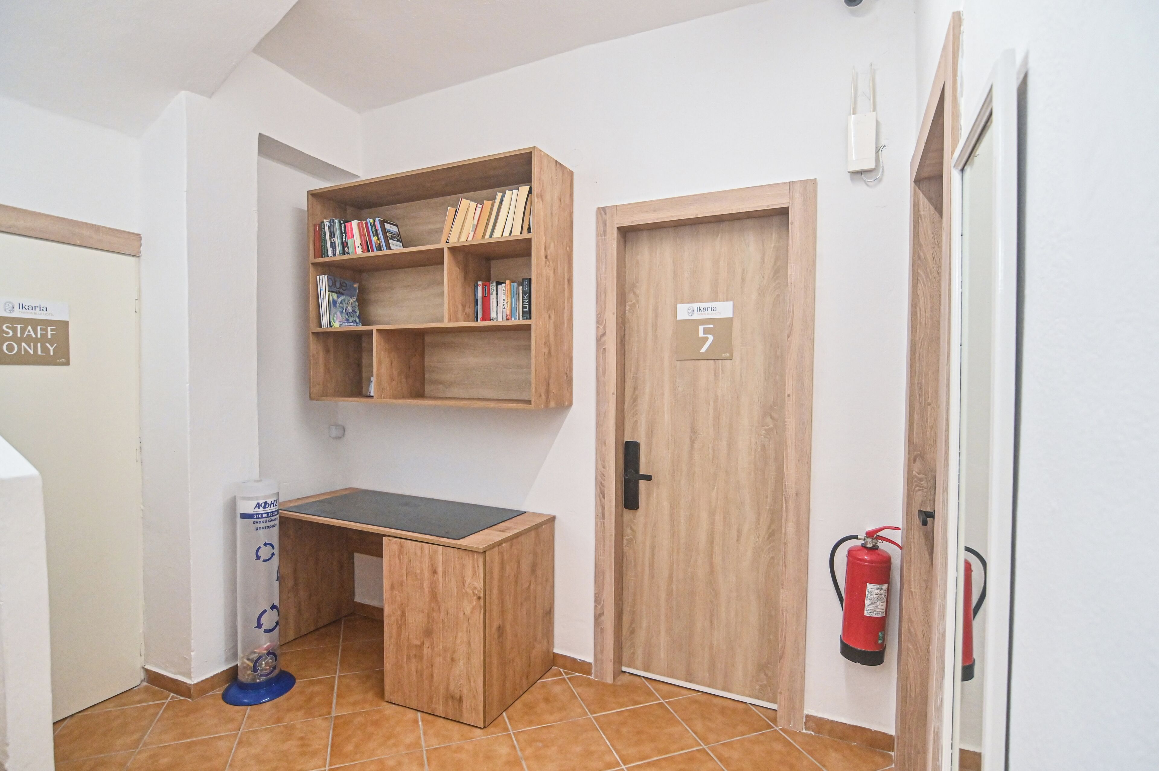 Une pièce avec un bureau en bois, une bibliothèque, une porte portant l’inscription « 5 », un extincteur et un panneau indiquant « accès réservé au personnel ».
