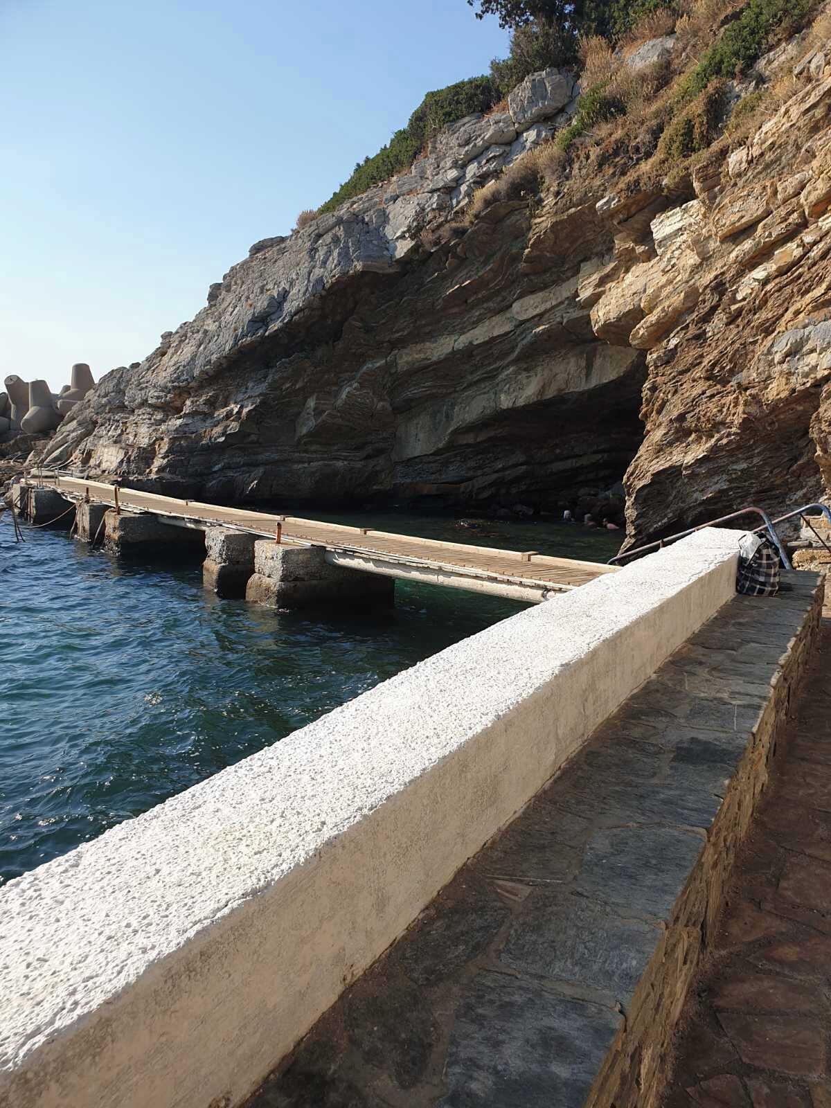 A coastal stone bridge over water, with rocky cliffs and sparse vegetation.