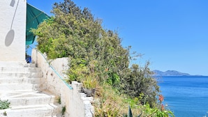 A coastal staircase with steps leading down to a body of water, surrounded by vegetation and a clear sky.