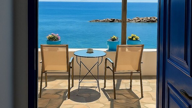 A view from a balcony with a pergola, a table, two chairs, and potted plants.