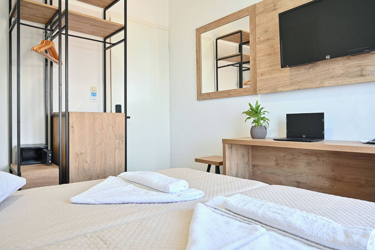 Ein Hotelzimmer mit Bett, Schreibtisch, Laptop, Fernseher, Pflanze und Spiegel.