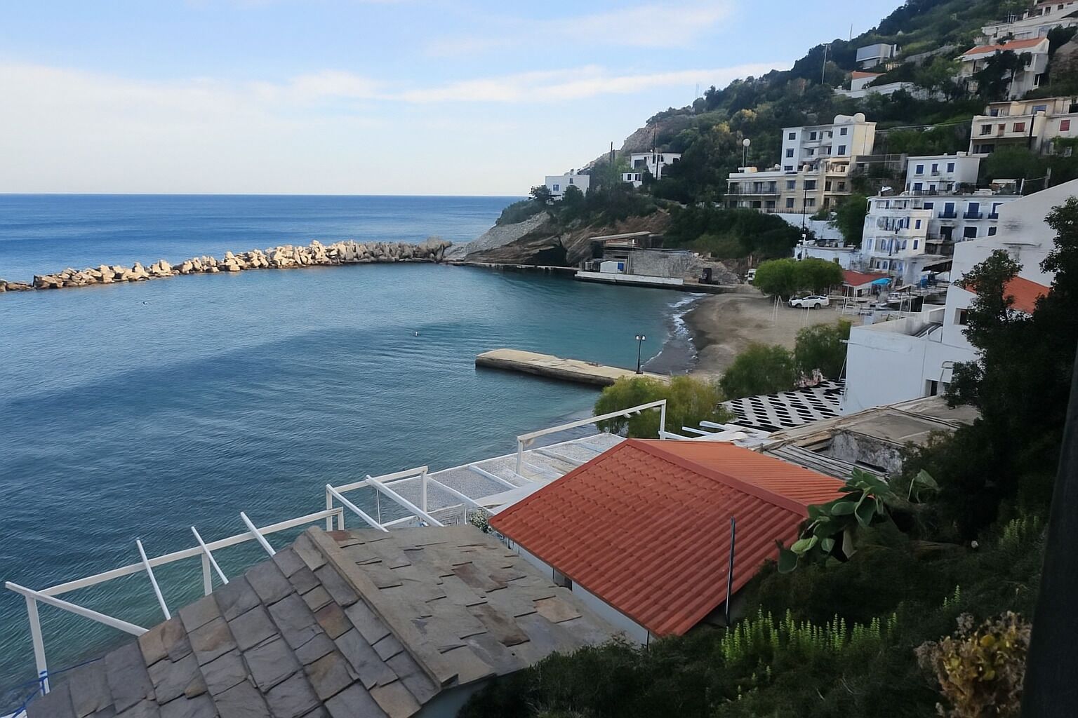 A coastal town with a rocky shoreline, buildings with red-tiled roofs, and a clear view of the sea.